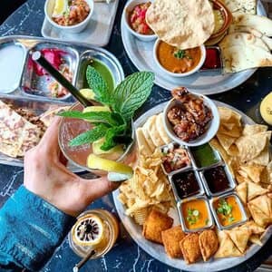 cun-food-and-drinks Indian Fast Casual Restaurant Hand holding drink and platters of food at franchisee location