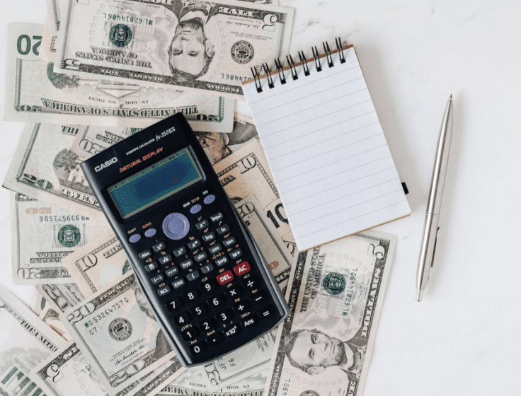 franchise business fees image of a calculator and note pad on top of a pile of cash