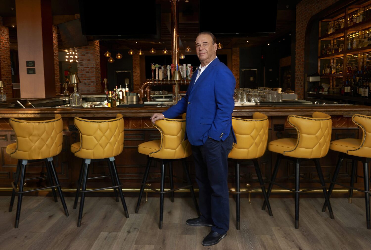 Image of a man in blue suit jacket standing at a dark bar