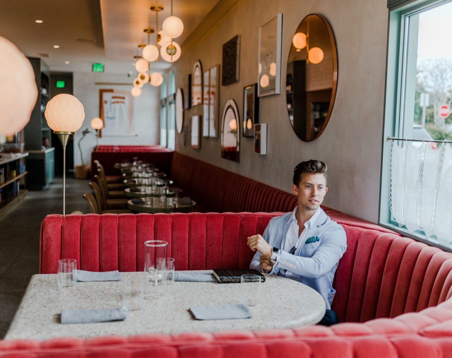 Young man in pale blue suit sitting at a red booth in restaurant