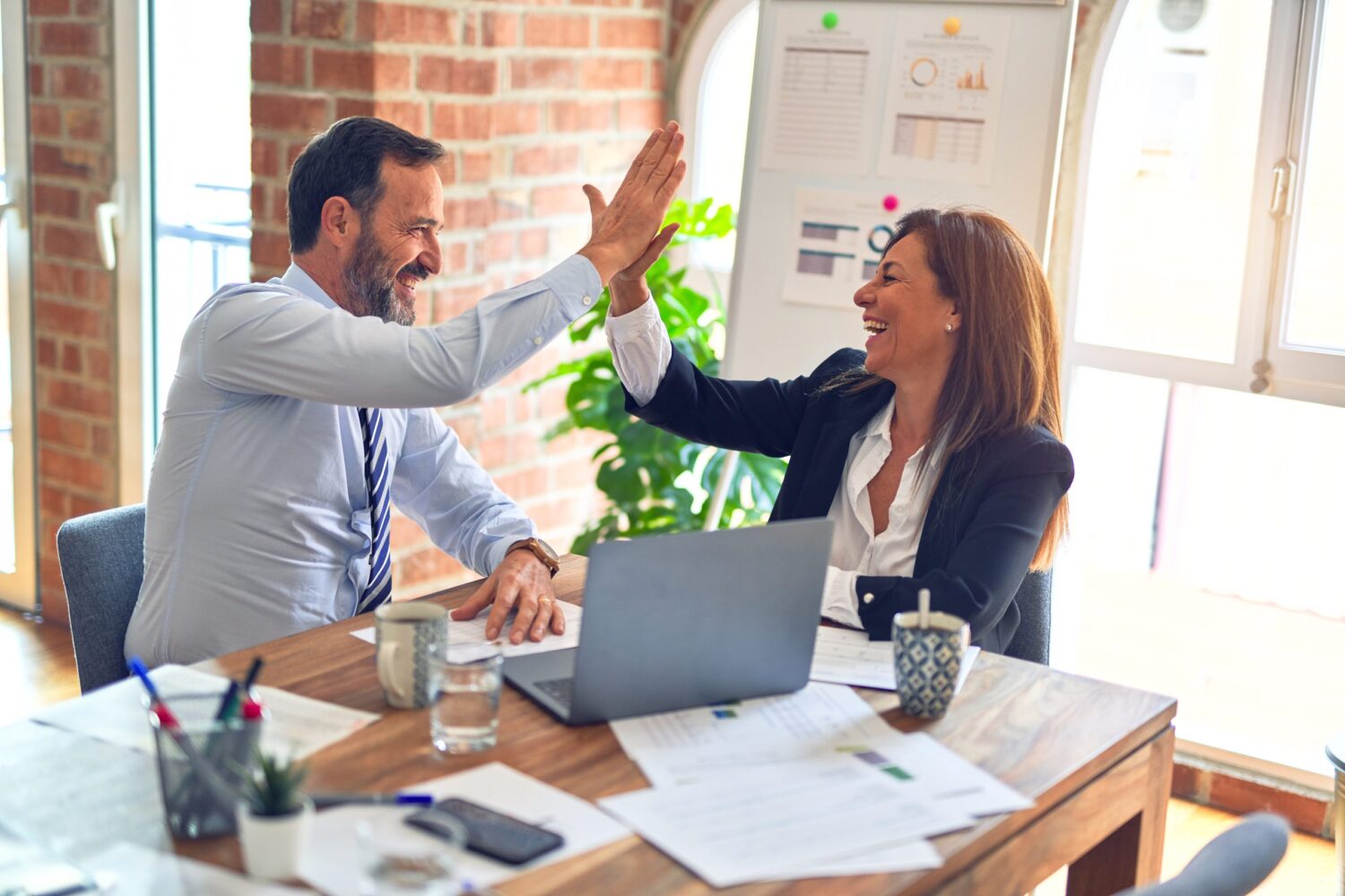 A business man and woman sitting at a desk high fiving each other
