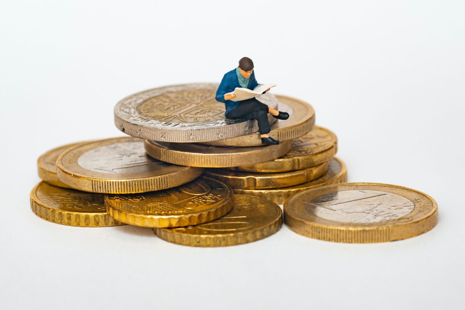 Miniature man with legs crossed sitting on a stack of large golden coins