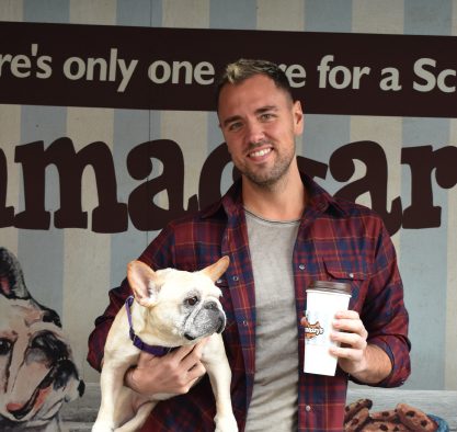 Man in red flannel holding a coffee and a white dog 