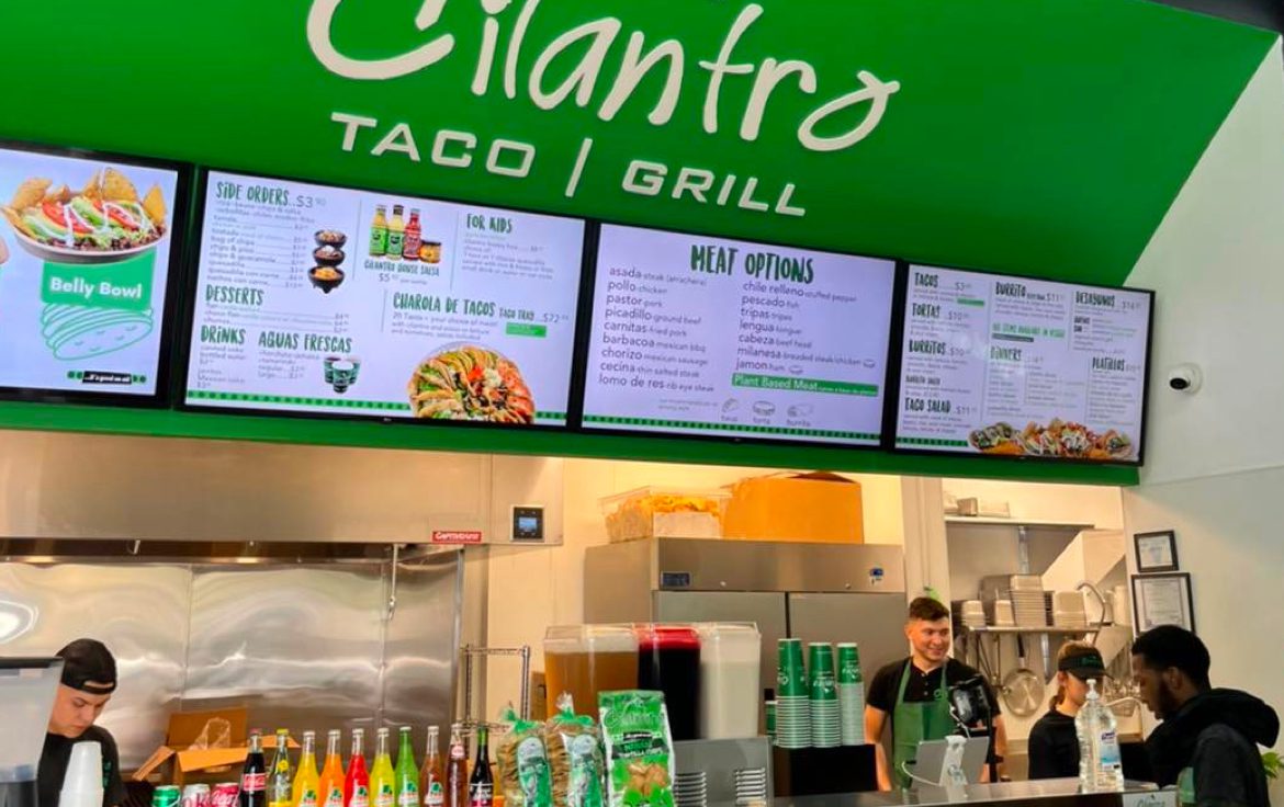 Fast food counter with a green Cilantro Taco Grill sign and food menus