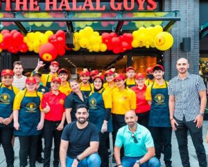 The Halal Guys franchise grand opening of a new store, with the team gathered outside underneath the building sign
