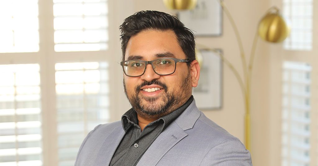 Headshot of North Carolina Curry Up Now Franchisee Pathik Patel. Wearing gray suit and glasses, background is a living room.