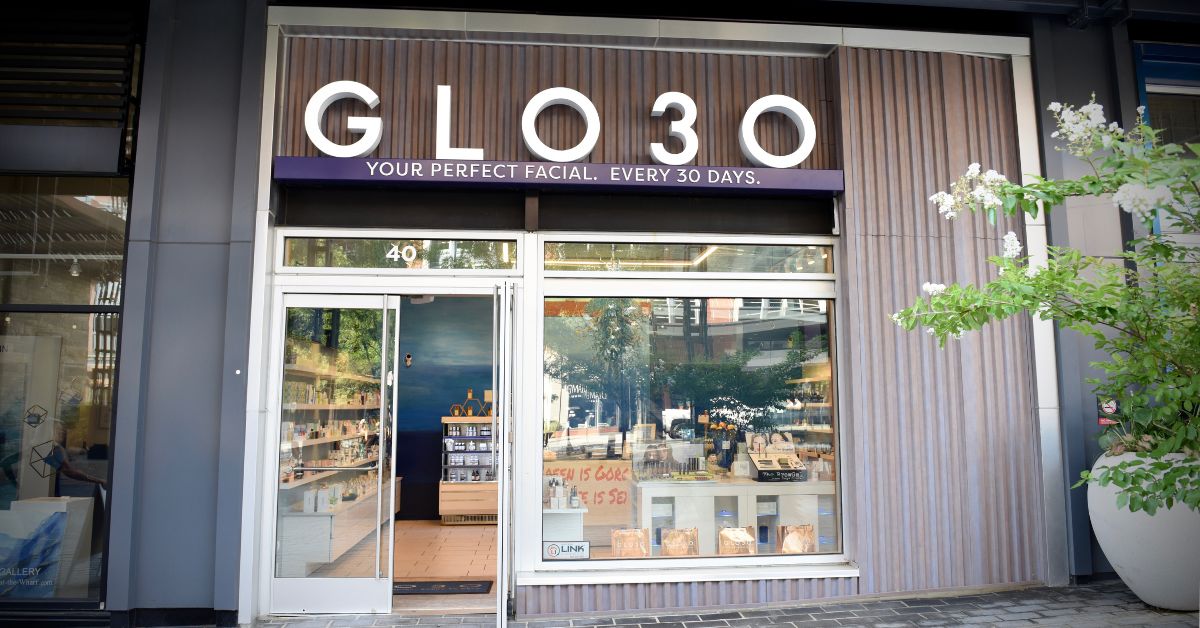 A storefront with dark wood slats on its exterior. In white lettering, the sign reads 'GLO30. Your perfect facial. Every 30 days.' The entrance consists of glass doors with window panels. glo30 membership based skincare studio headlines may 2024